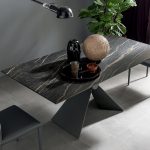 Photo d'une table rectangulaire. Pied central en métal avec une forme en V. Table avec plateau céramique noir veine beige.