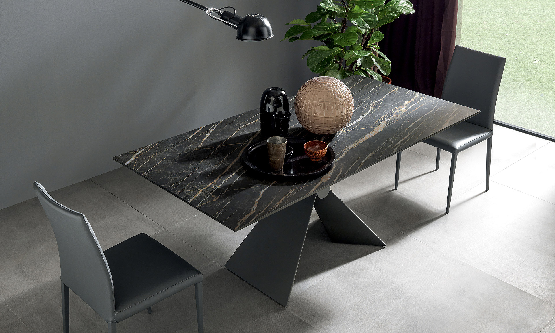 Photo d'une table rectangulaire. Pied central en métal avec une forme en V. Table avec plateau céramique noir veine beige.